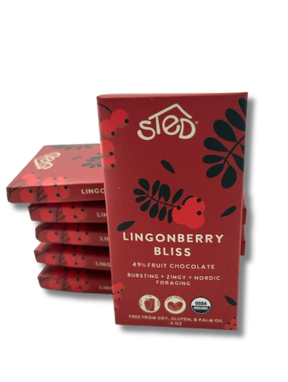 A stack of red packages labeled Sted Lingonberry Bliss with icons for 49% fruit, dairy free, soy free, gluten free, USDA organic, and lingonberry fruit chocolate bar.