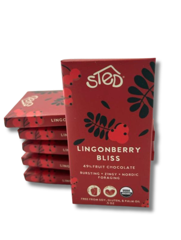 A stack of red packages labeled Sted Lingonberry Bliss with icons for 49% fruit, dairy free, soy free, gluten free, USDA organic, and lingonberry fruit chocolate bar.