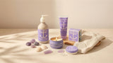 A lavender-themed skincare set featuring Sea Salt Lavender Swedish Dream Bar Soap—Triple Milled Natural Lavender 4 oz—plus hand soap, hand cream, a candle, and a tin, arranged with shells and stones on wood and fabric.
