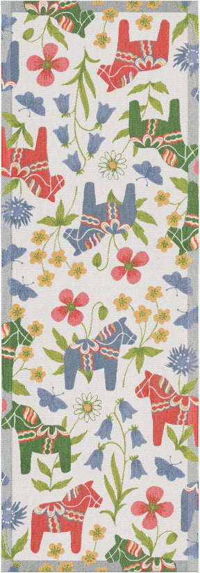 The "Blomsterhast" Flower Horse Table Runner by Ekelund is a rectangular organic cotton runner with red and blue Swedish Dala horses, green leaves, and colorful flowers on a white background.