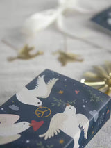 Dark blue wrapping paper with a white Scandinavian-style pattern of doves with olive branches, peace signs, hearts, and stars.