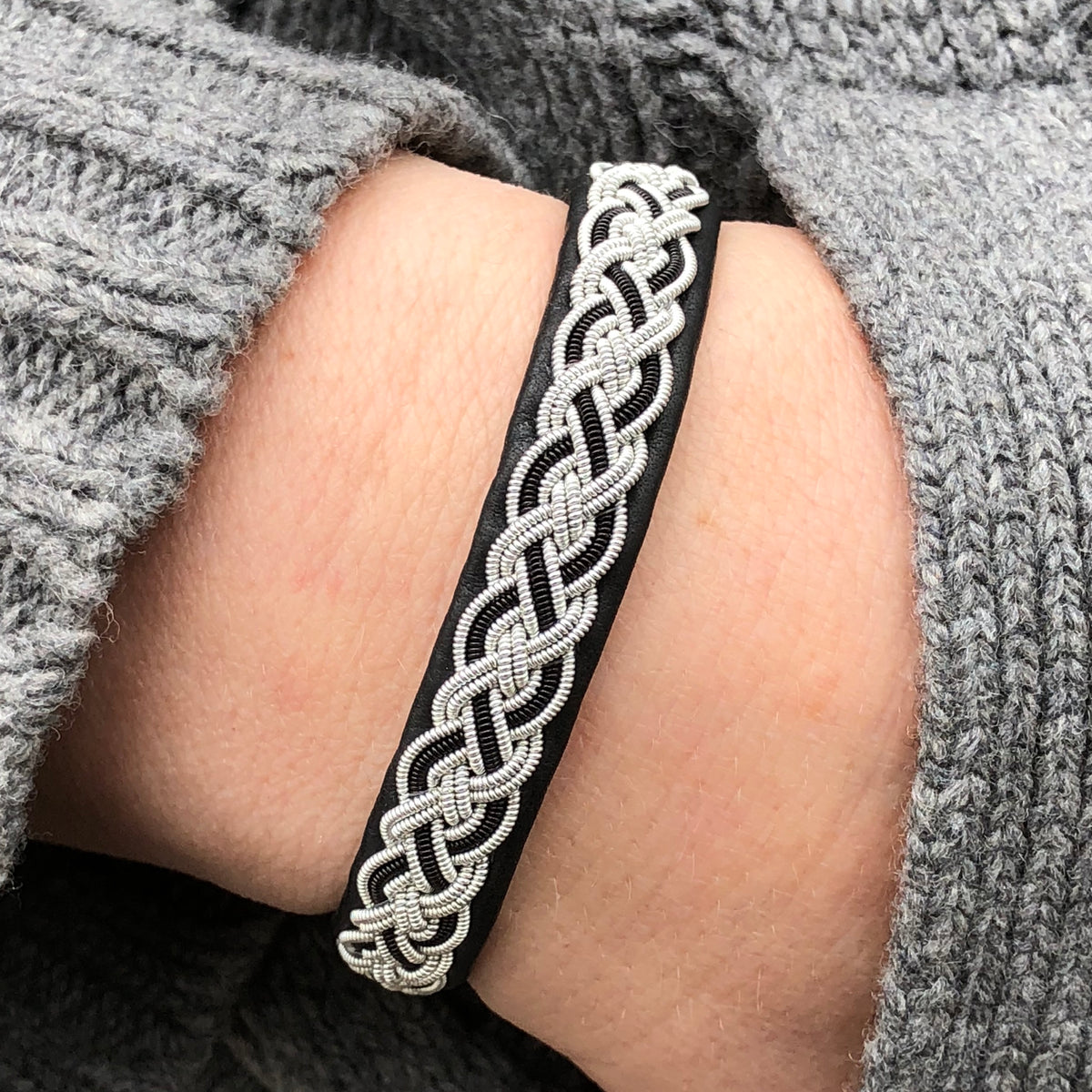 The Sami Alice Black Bracelet, featuring intricate silver braids and a reindeer antler button clasp, is elegantly worn on the wrist.