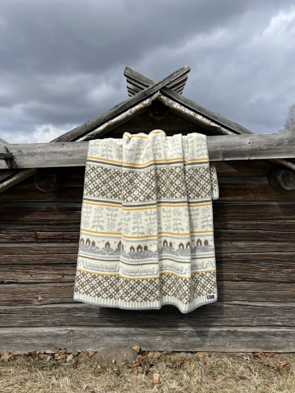 A Bohus blanket, made of 100% Norwegian lambs wool by Kerstin Landstrom, with geometric patterns hangs over a wooden fence. The overcast sky enhances the cozy charm of this Norwegian-inspired piece.