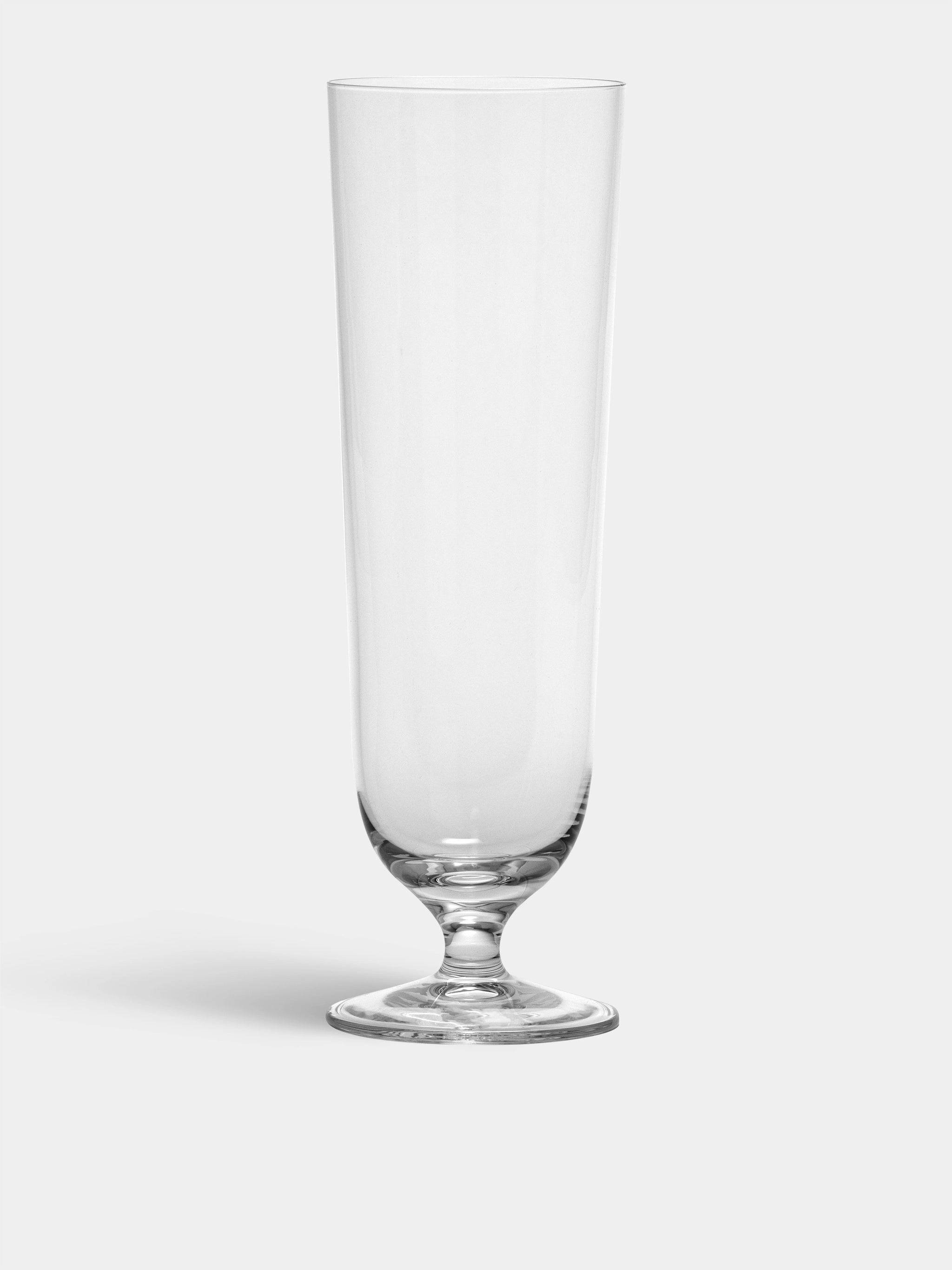 A tall, clear Orrefors Beer Pils glass from the 15.5oz (4-Pack) by Erika Lagerbielke features a short stem and round base, standing elegantly against a plain background.