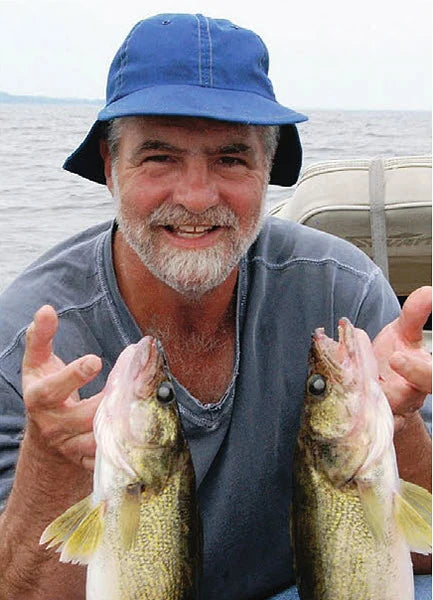 Man in a blue hat holding two large fish on a boat with water in the background; design featured on a jigsaw puzzle.