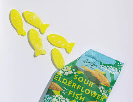 Five yellow, fish-shaped sour gummies from the Bundle: BonBon Sour 4-Pack – The Ultimate Swedish Fish Reimagined spill from a partially opened package, offering a gourmet candy twist to the classic treat on a white background.