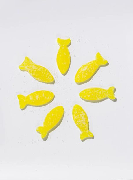 Seven yellow candies from the Bundle: BonBon Sour 4-Pack – The Ultimate Swedish Fish Reimagined are arranged in a circle on a white background, each dusted with sugar and reminiscent of classic Swedish Fish.