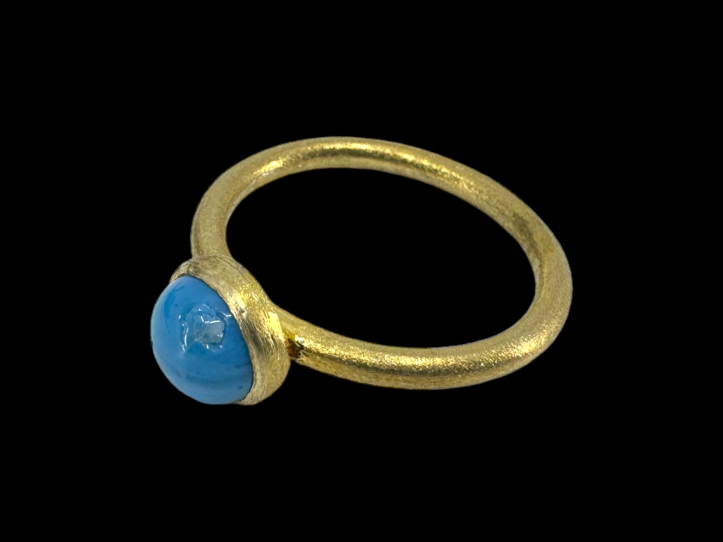 The Cirkel Gold - Swedish Blue ring showcases a smooth, round Swedish Blue stone elegantly set at the center, all highlighted against a sleek black background.