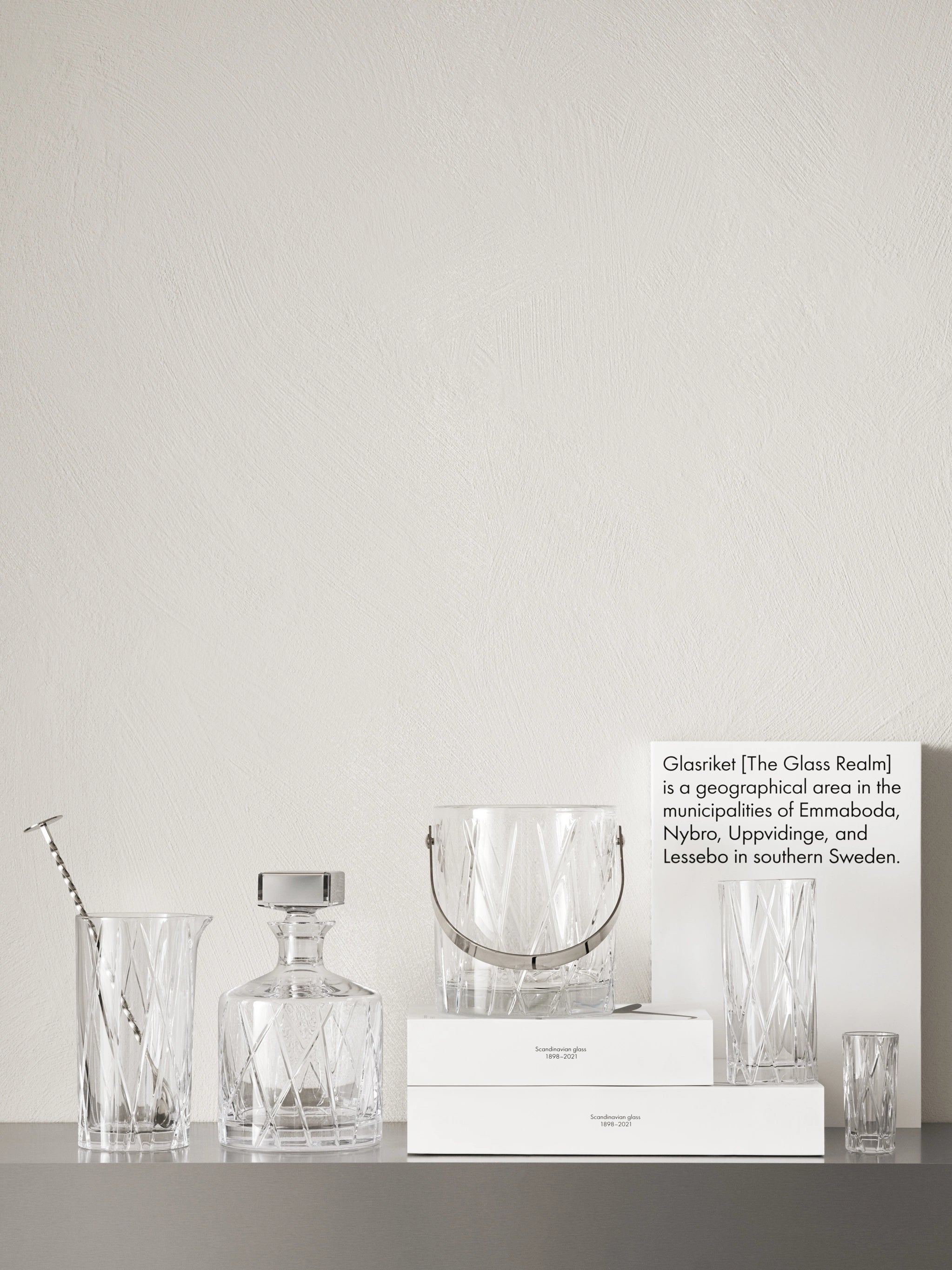 The Orrefors City Mixing Glass with Spoon 22oz and a decanter are elegantly displayed on a surface alongside an information sign about Glasriket, a renowned area in southern Sweden.