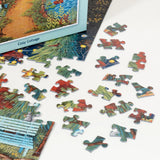 Colorful puzzle pieces scattered beside a cottage-shaped puzzle box decorated with Scandinavian folk art motifs, all displayed on a white surface.