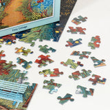 A partially completed PuzzleTwist Something's Amiss! Cozy Cottage 500 Piece puzzle by artist Mary Charles lies on a white surface, with several loose pieces spread nearby and its box visible.