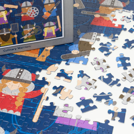 Jigsaw puzzle pieces showing cartoon Viking chefs with kitchen tools; puzzle box in the upper left displays Cindy Lindgren’s Scandinavian art.