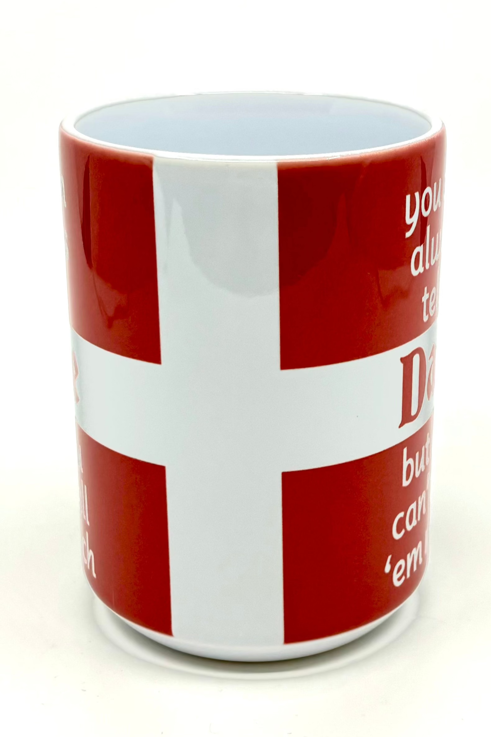 The "You Can Tell a Dane" mug is a red 15 oz cup adorned with a white cross design similar to the Danish flag, with partially visible text on the sides.