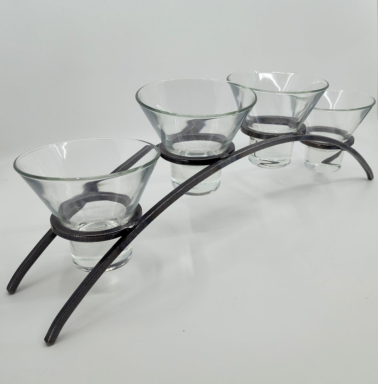 The Danish Iron Arched Candle Holder elegantly supports 4 Leif Cups, perfect for ball candles, on a graceful curved metal stand with two sturdy legs.