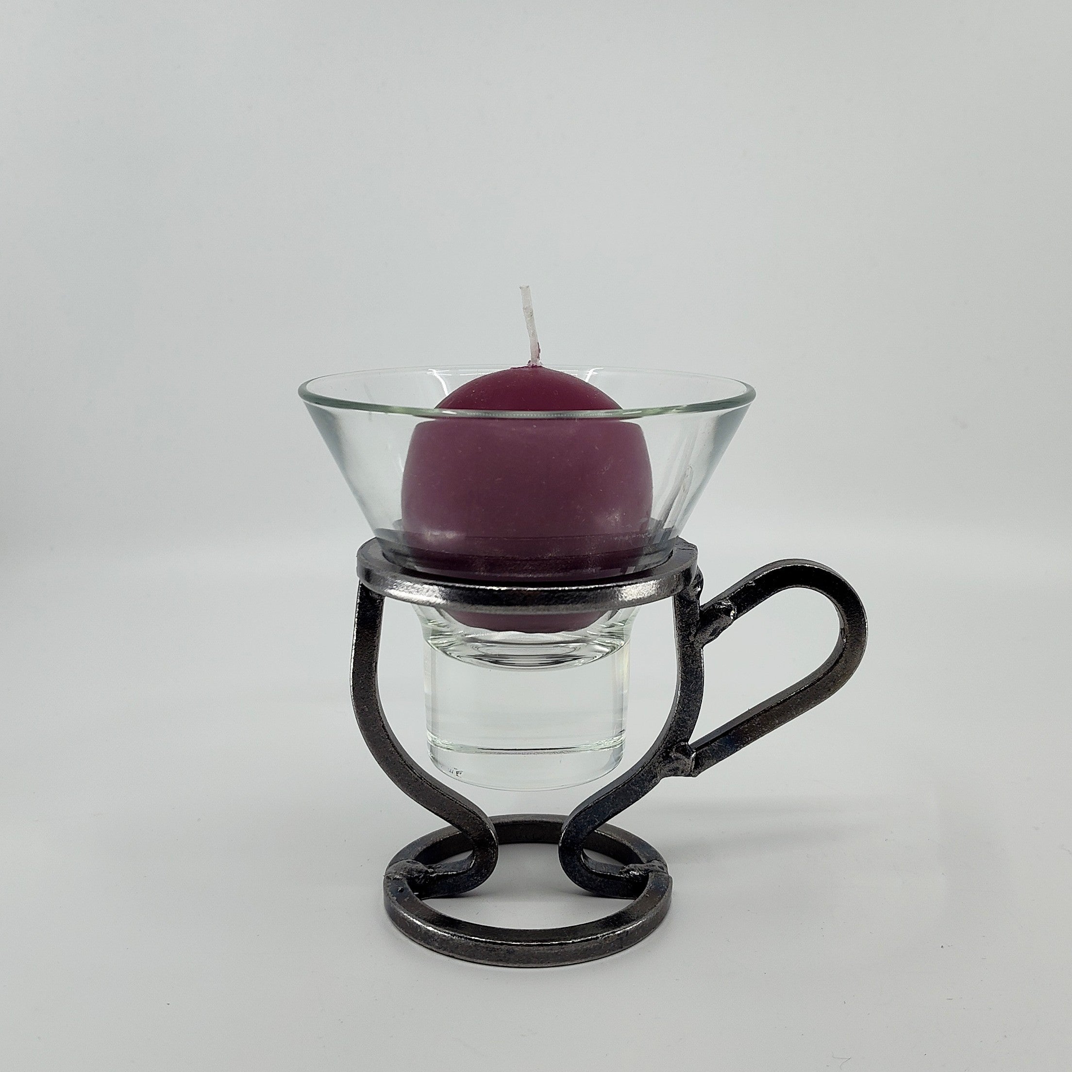 A purple candle elegantly rests in a Danish Iron Coffee Cup with Leif Glass Cup, resembling a delicate cup.