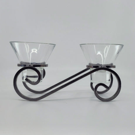 The Danish Iron Candleholder features two Leif glass cups for ball candles, elegantly mounted on a decorative black wrought iron stand with an artistic swirl design, set against a plain gray background.