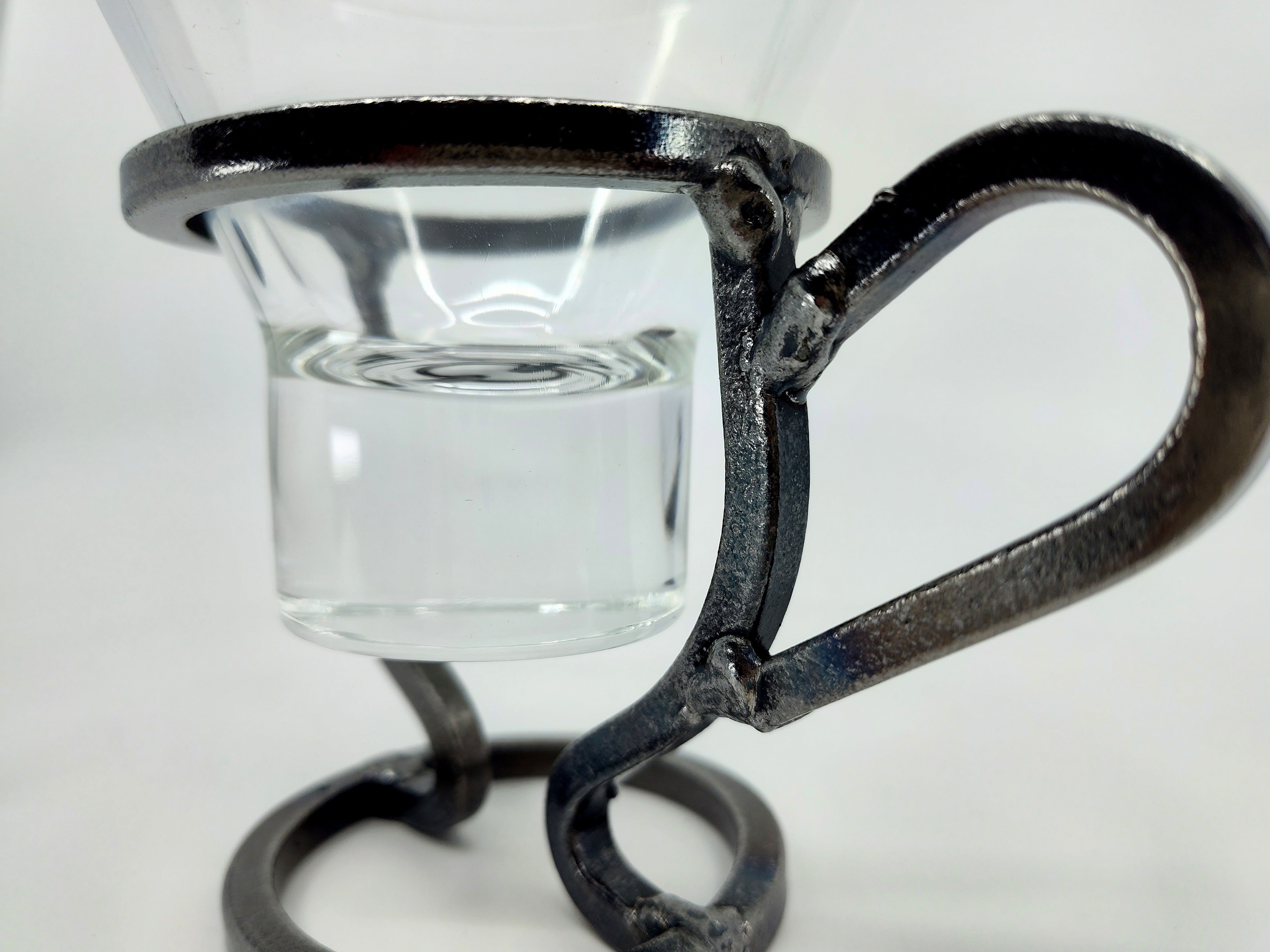 A Leif Glass Cup is stylishly embraced by a metallic handle on the Danish Iron Coffee Cup, crafted as a candle holder for ball candles, against a white background.