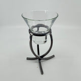 A clear glass bowl rests elegantly on a Danish Iron Candle Holder with a crossed iron base and cup for a ball candle, set against a plain white backdrop.