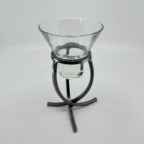 A clear glass bowl rests elegantly on a Danish Iron Candle Holder with a crossed iron base and cup for a ball candle, set against a plain white backdrop.