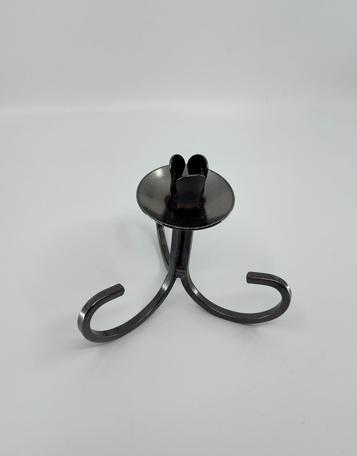 The Danish Iron Taper Candleholder, with a curly bottom and sleek black metal design, features three graceful legs and a round base, ideal for elegantly displaying tapered candles.