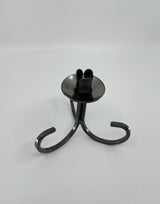 The Danish Iron Taper Candleholder, with a curly bottom and sleek black metal design, features three graceful legs and a round base, ideal for elegantly displaying tapered candles.