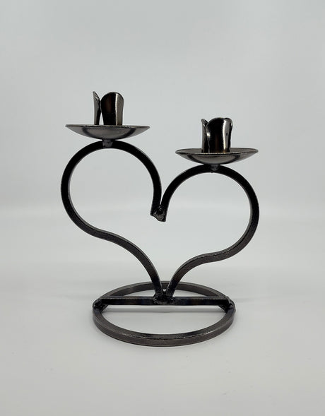 The Candle Holder: Danish Iron Taper Candleholder, featuring a large heart and slots for two taper candles, sits on a sturdy circular base against a plain white background.