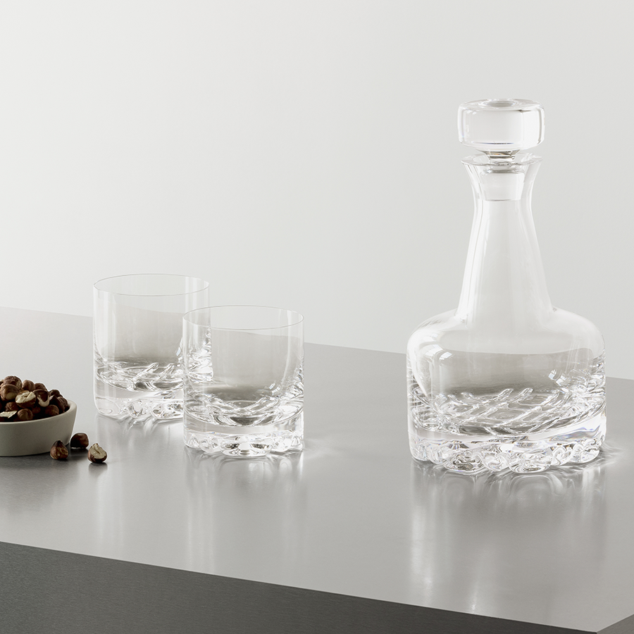 An Orrefors Erik Double Old Fashioned Glass 12oz (4-Pack) set enhances the countertop with Scandinavian elegance, ideal for whiskey lovers. A small bowl of nuts adds a perfect complement to this sophisticated display.