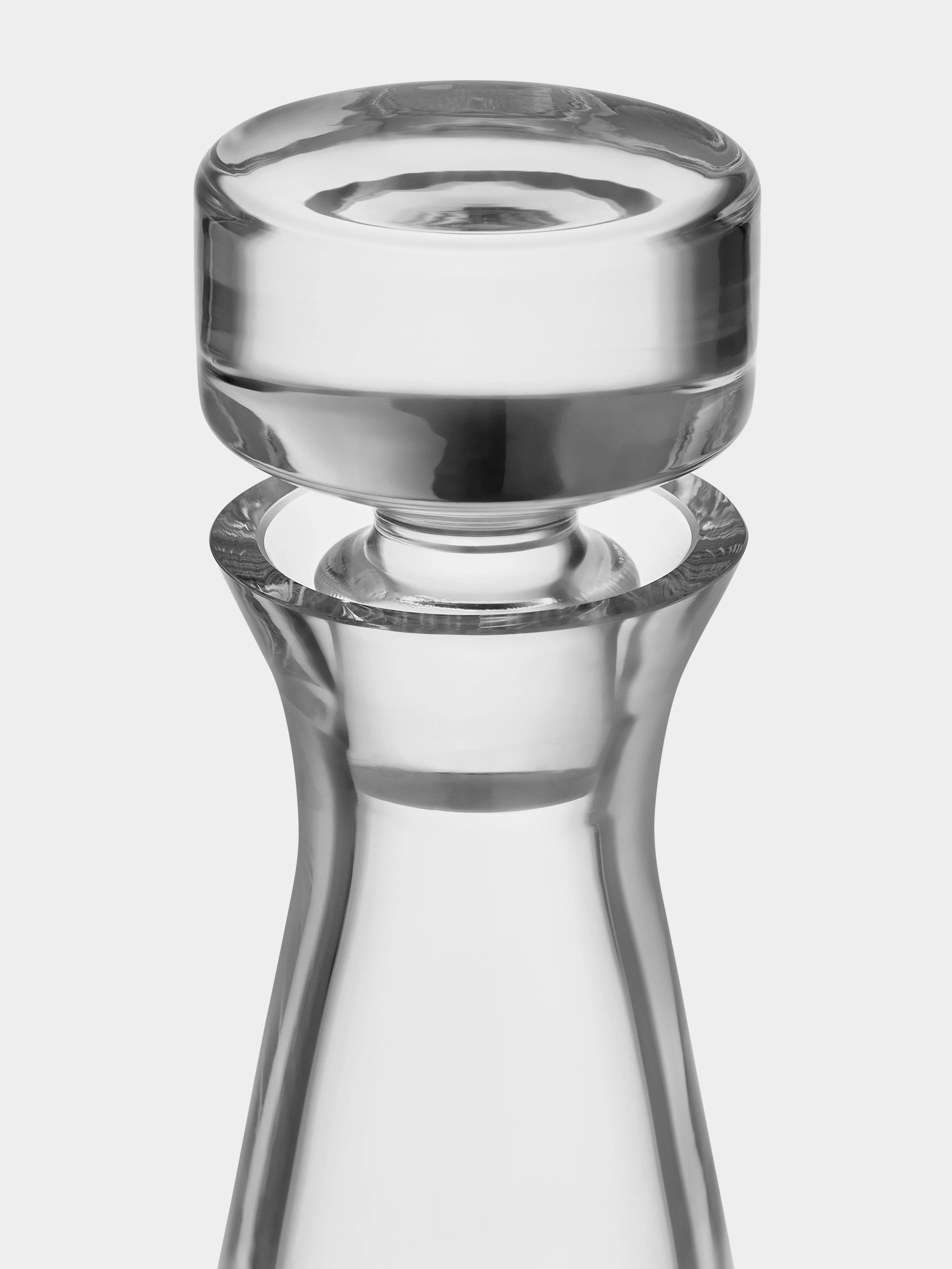 A close-up of an Orrefors Erik 26oz decanter from the 3-piece set, featuring a clear glass bottle neck with a round, flat stopper, reminiscent of a classic style.