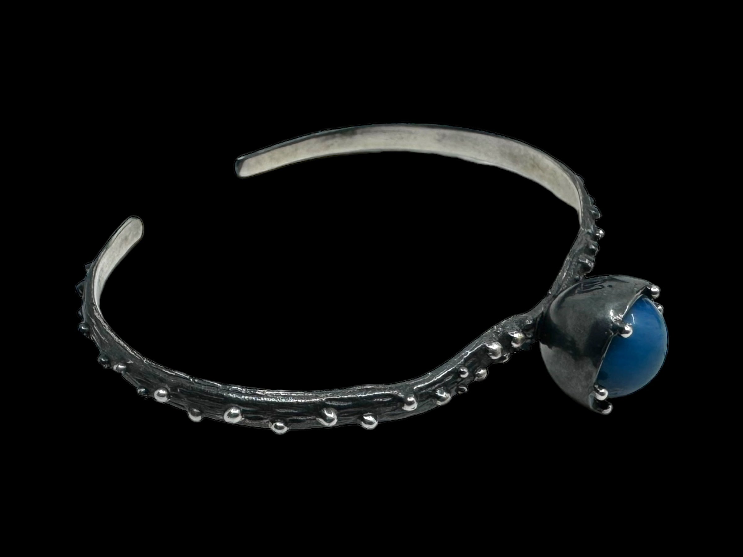 The Freja Thin bracelet features an oxidized silver design, elegantly showcasing a Swedish Blue ball set within a claw-like motif.