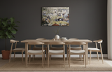 A modern dining room features a wooden table with six chairs, a potted plant, a neutral rug, and the "Artwork: The Crayfish Season Opens Carl Larsson 1897 Print on Canvas" displayed on the dark gray wall.