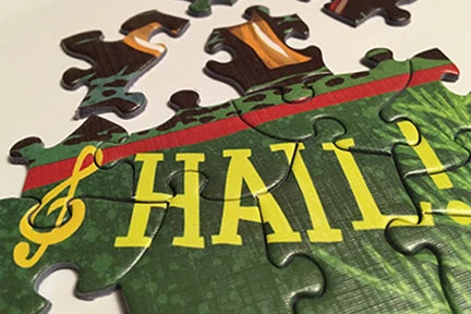 Close-up of a jigsaw puzzle with green and yellow pieces, the word “HAIL!”, a treble clef symbol, and several missing pieces shown in Adam Turman’s art style.
