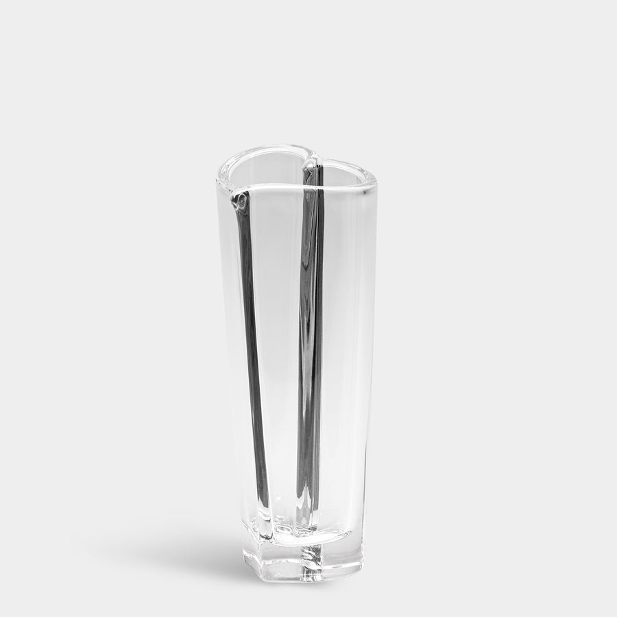 The Orrefors Heart Bud Vase is a clear, tall heart-shaped crystal vase with a smooth surface, elegantly standing on a plain white background.