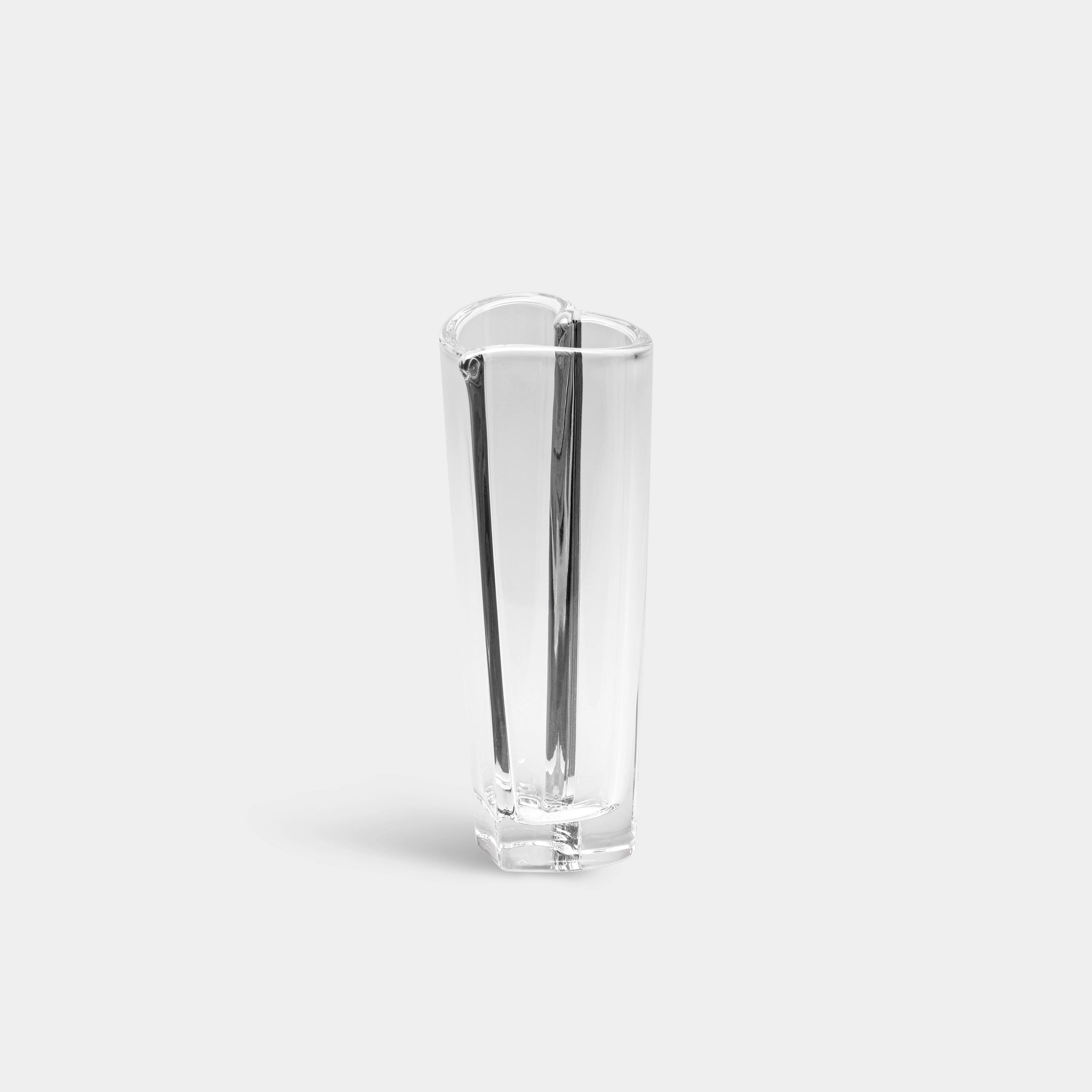 The Orrefors Heart Bud Vase, a tall crystal glass with a modern asymmetric design, highlights elegance against a light gray backdrop.