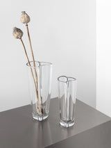 Two Orrefors Heart Bud Vases sit on a gray surface, with the larger one holding two dried poppy seed pods.