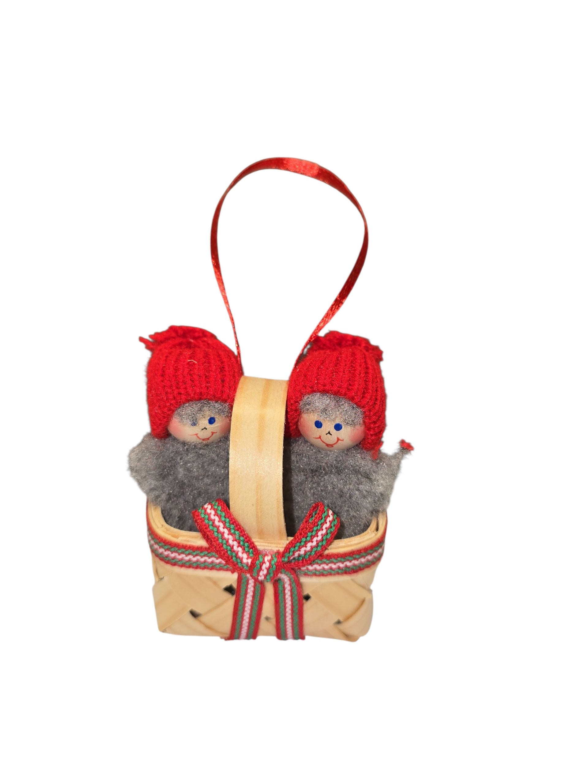 The Ornament: Swedish Santa Figurines in a Basket features two dolls in red knit hats and gray scarves, handmade to capture Scandinavian holiday charm with a ribbon and red hanging loop.