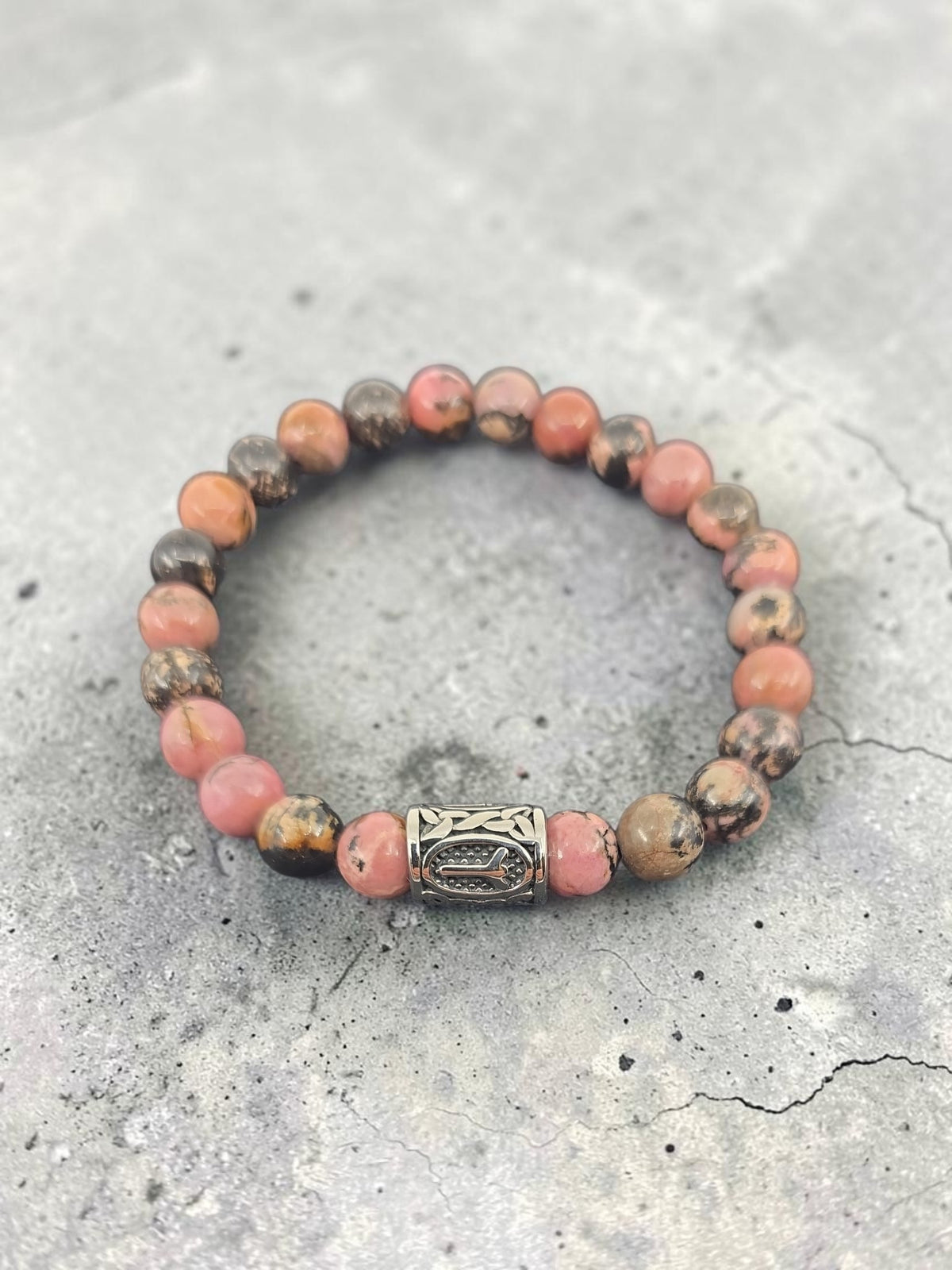 Beaded bracelet with pink and brown stones, decorative silver clasp, displayed on a textured gray surface.