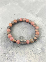 Beaded bracelet with pink and brown stones, decorative silver clasp, displayed on a textured gray surface.