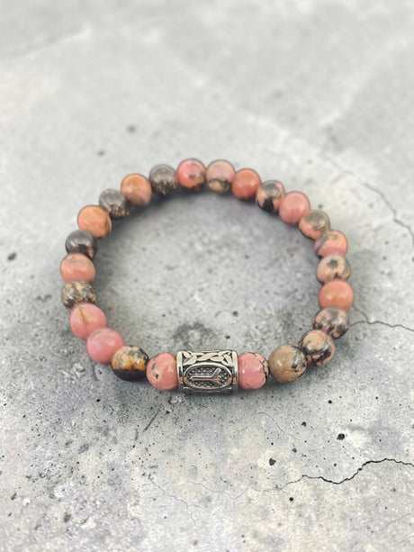 Beaded bracelet with pink and brown stones, decorative silver clasp, displayed on a textured gray surface.