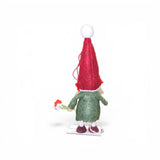 The Faire - Nordic Dreams "Figurine: Scandinavian Girl Tomte - Gnome Holding Flowers" is a small, handcrafted Nordic figurine with a tall red hat, green coat, white shoes, and a red-and-white flower, facing away on a white background.