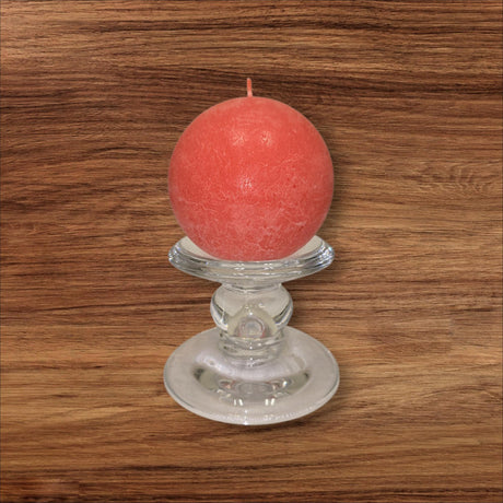 A round red candle rests on the Glass Dual-Size Reversible Candle Holder, designed for taper, ball, or pillar candles, displayed on a wood surface with visible grain.