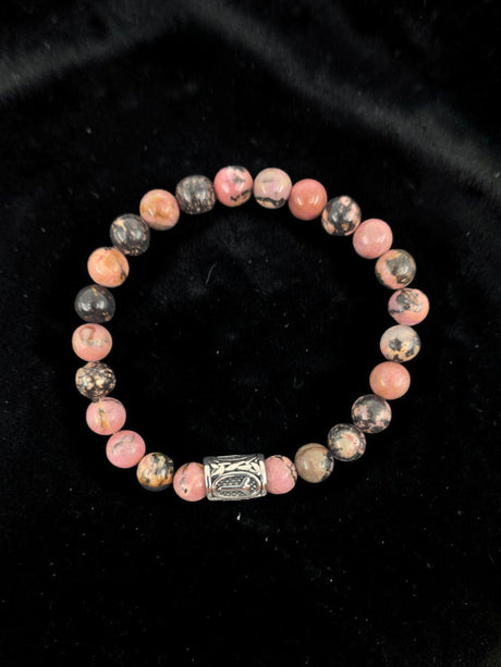 Bracelet with pink and black marbled round stones and a single silver bead, displayed on black velvet.