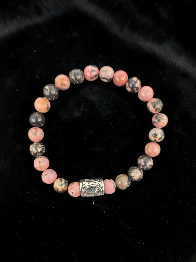 Bracelet with pink and black marbled round stones and a single silver bead, displayed on black velvet.