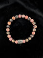 Bracelet with pink and black marbled round stones and a single silver bead, displayed on black velvet.