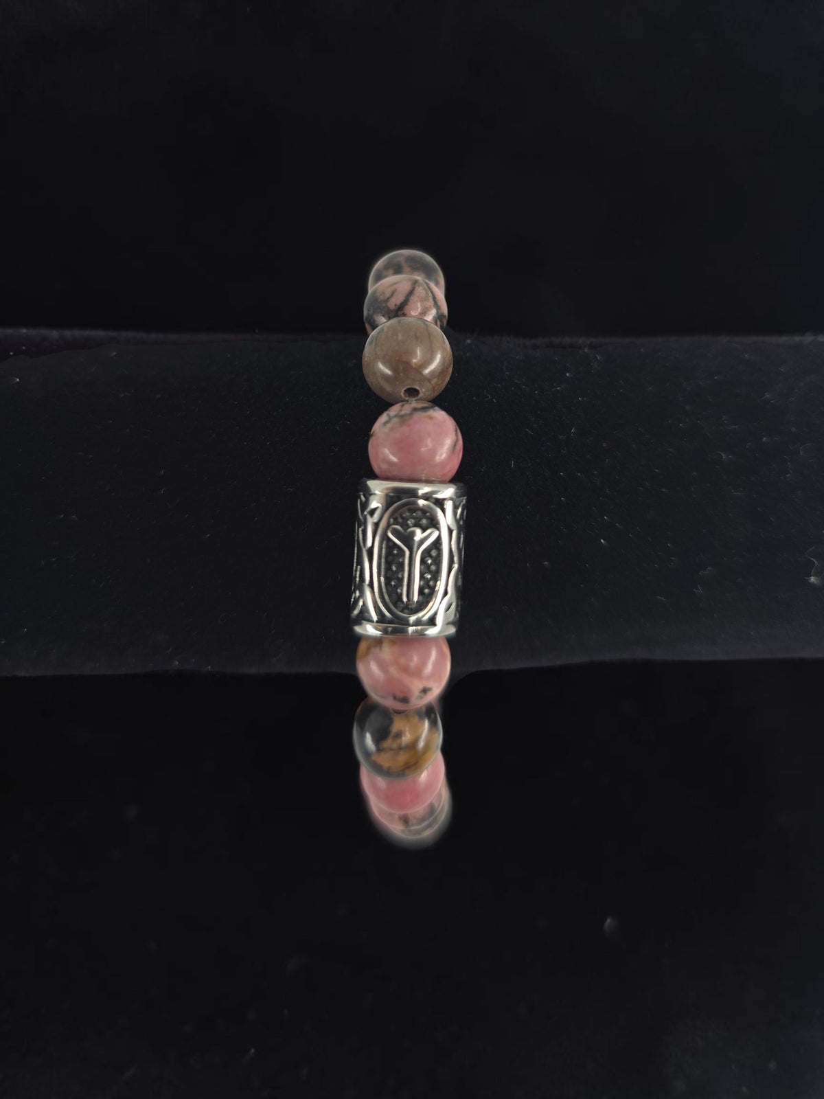 Beaded bracelet with pink, brown, and clear round beads and a central silver bead engraved with the Algiz rune, shown on a black velvet display stand.