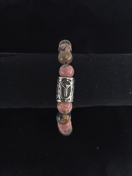 Beaded bracelet with pink, brown, and clear round beads and a central silver bead engraved with the Algiz rune, shown on a black velvet display stand.