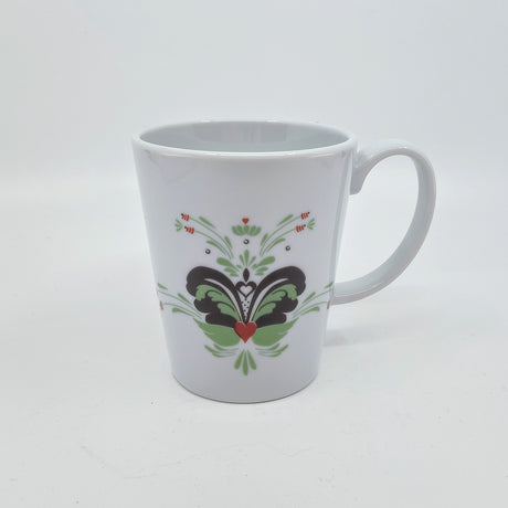 The "Coffee Mug: Anna Viktoria Porcelain Mug with Light Green, Grey, and Red Kurbits" features a handle and a symmetrical Swedish kurbits floral and heart design on the front. The mug is displayed against a plain white background.