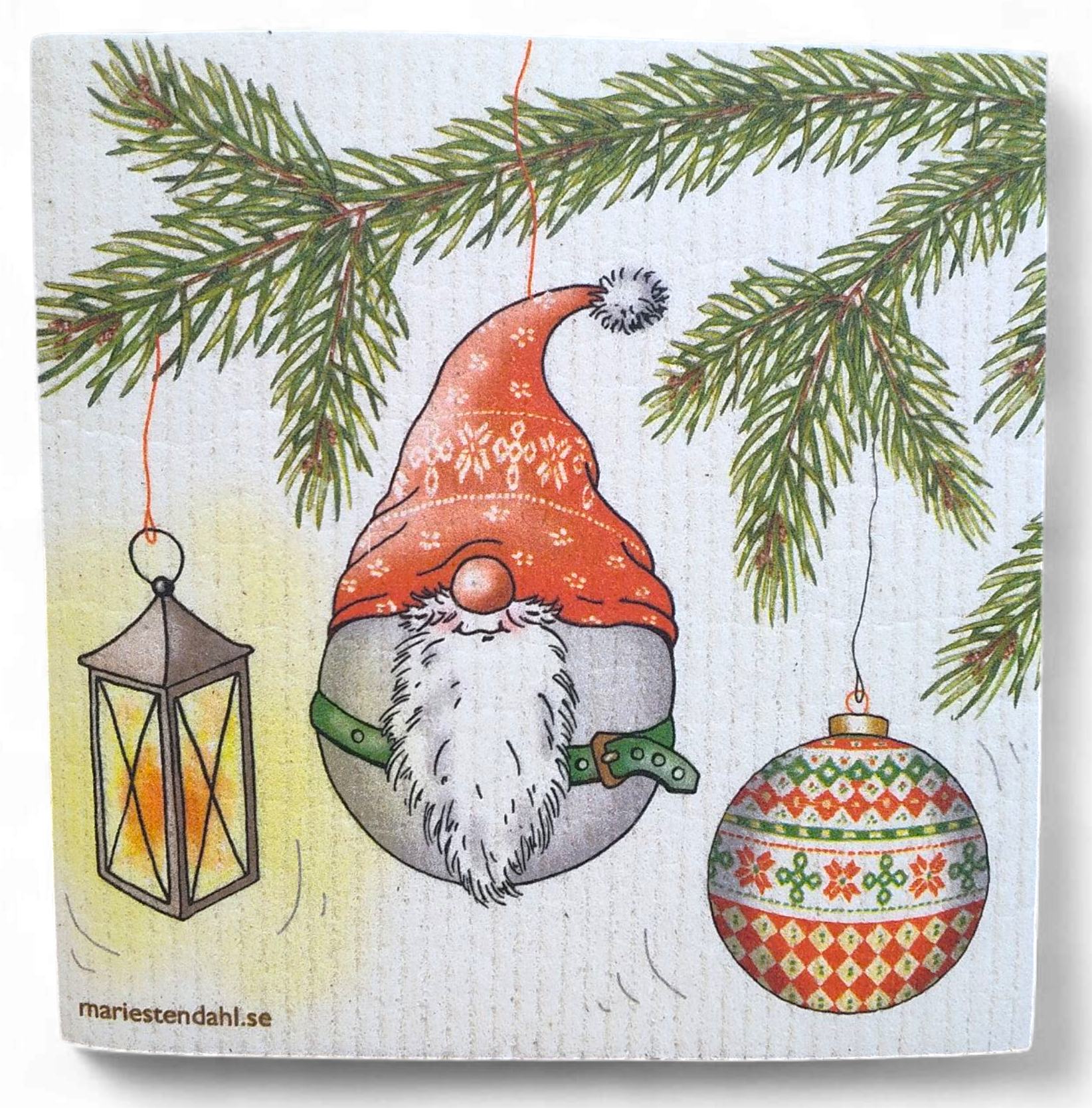 The Dish Cloth: Holiday Ornament Design by Marie Stendahl features a festive lantern, red-hatted gnome, and patterned ornament hanging from pine branches on an eco-friendly Swedish dish cloth.