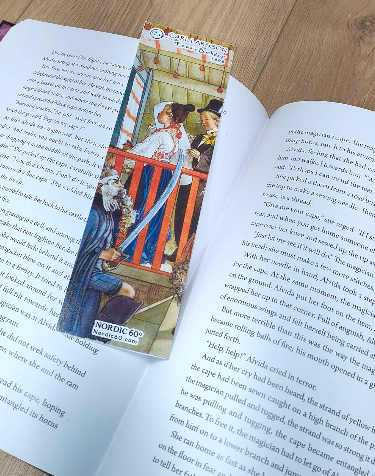 An open book rests on a wooden surface, marked by the “Emma’s Birthday” Carl Larsson bookmark (8.5" × 2.5"), inspired by Swedish art—a charming Scandinavian gift featuring a historical scene.