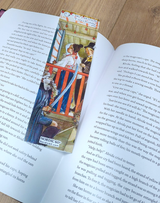 An open book rests on a wooden surface, marked by the “Emma’s Birthday” Carl Larsson bookmark (8.5" × 2.5"), inspired by Swedish art—a charming Scandinavian gift featuring a historical scene.