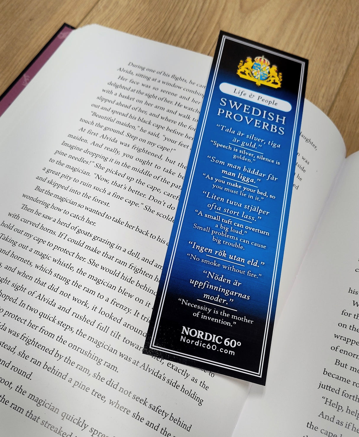 A set of 4 bookmarks titled "Bookmark: Set of 4 Swedish Proverbs (2.5\" × 8.5\")" displays Scandinavian wisdom in Swedish and English on a wooden surface, resting on an open book.
